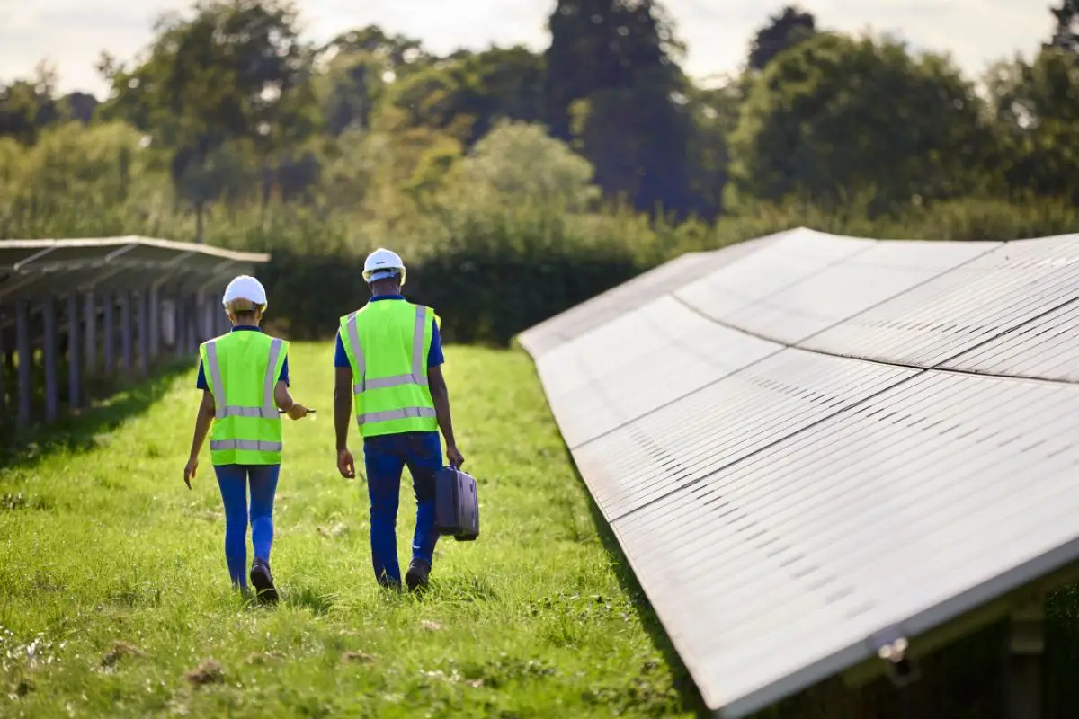 Zwei Fachkräfte begutachten eine große Solaranlage mit einem Tablet, unterstützt durch eine Drohne für detaillierte Analysen.